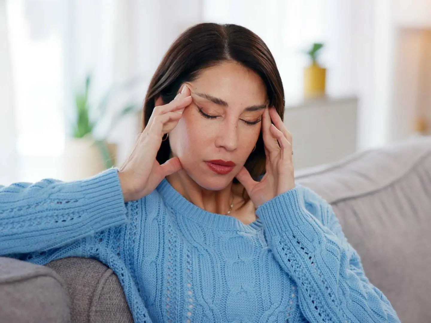 A woman on a couch battles brain fog with hands on her temples.