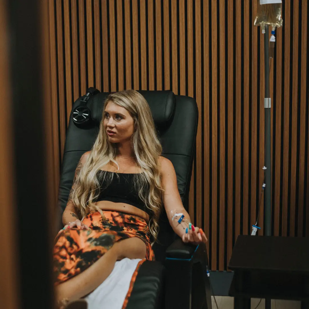 Blonde woman in black top and tie-dye skirt receiving NAD IV infusion
