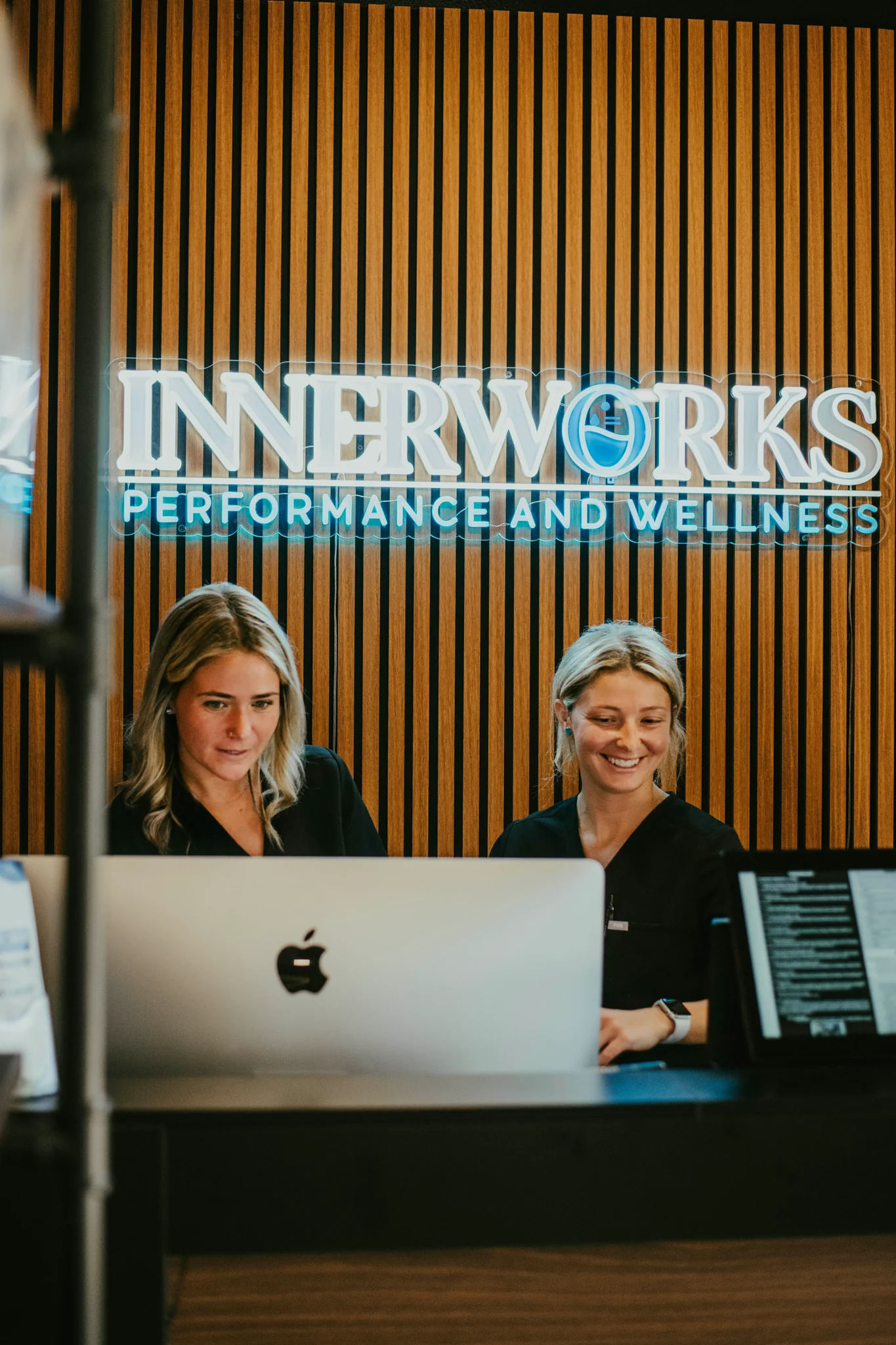 Two women smiling behind a desk at the reception of Innerworks Clinic