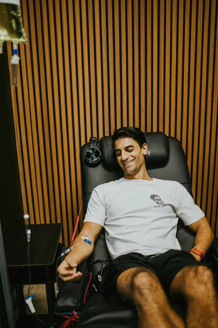 Smiling man receiving IV infusion in a black recliner chair with a drip bag and tube