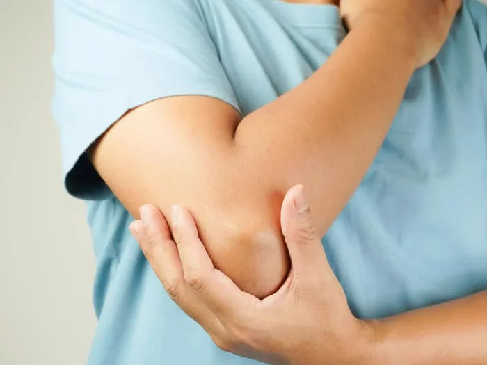 An injured person in a blue shirt holds their sore, inflamed elbow.