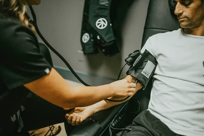 A medical professional takes a man's blood pressure using a cuff and stethoscope.