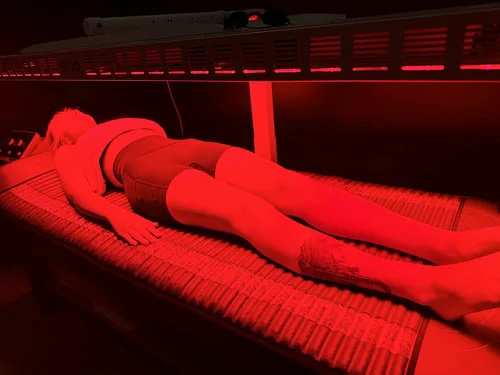 Person lying face down on a bed under red light therapy lamps.