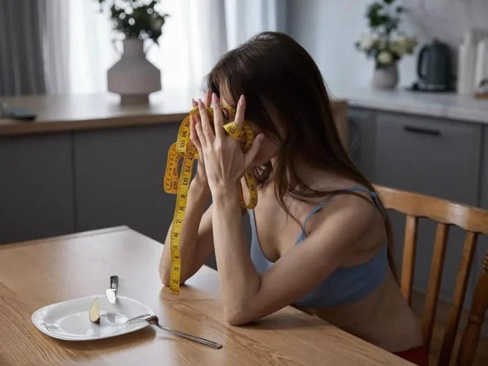 A woman with an apple fights nutrient deficiency behind a tape measure.