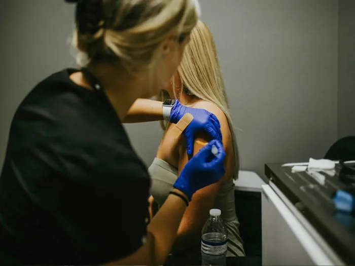 Medical professional administering an injection into a person's upper left arm.